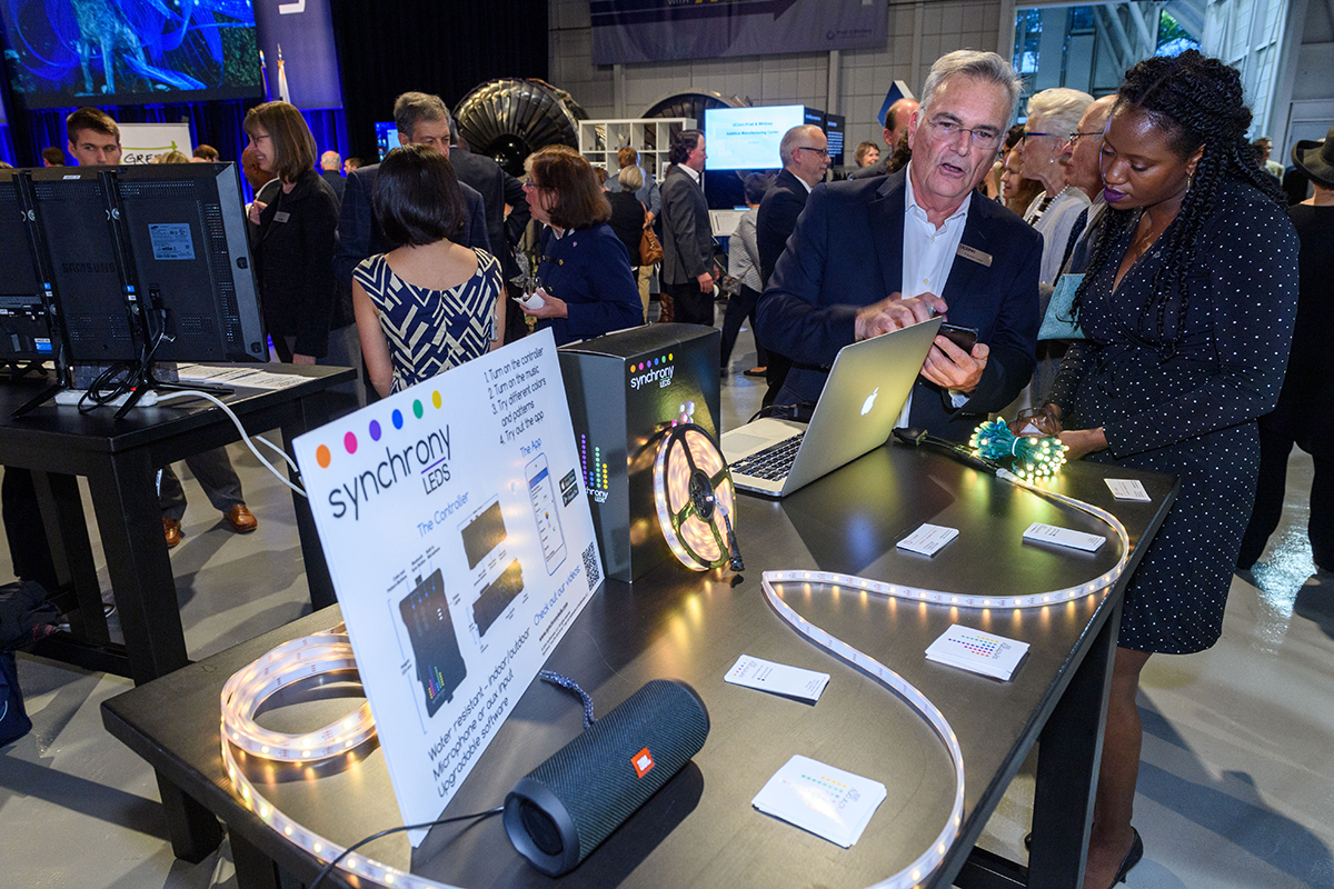 A professor of psychological sciences demonstrates a light show that simulates brain activity to an alumna at a crowded event.
